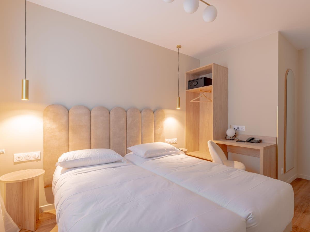 Chambre twin à la tête de lit cannelée, éclairée par ses suspensions dorées